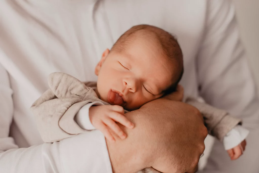 Un nouveau-né dans les bras de son papa et tirant la langue.